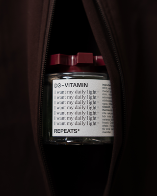 A clear jar of REPEATS D3-VITAMIN with a white label and a dark red cap, positioned inside a dark burgundy bag opening.