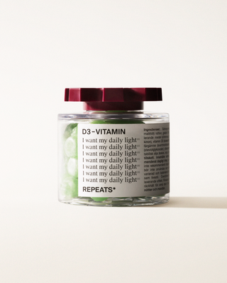 A transparent jar of REPEATS D3-Vitamin, filled with green gummies (supplements), sealed with a dark red, shaped lid. The jar has a white label featuring the text "D3-Vitamin", repeated rows of "I want my daily light", and the brand Logo
