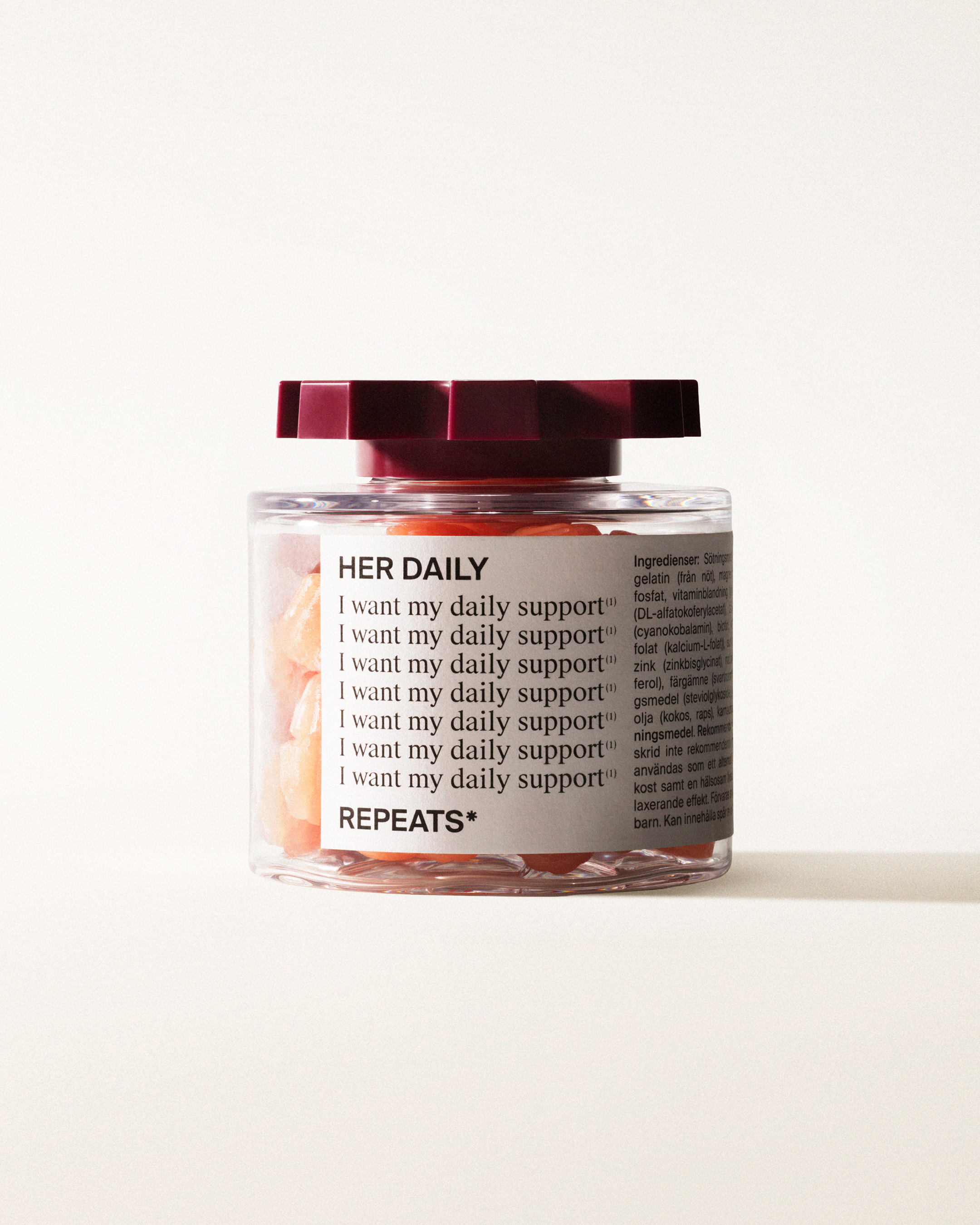 A transparent jar of REPEATS Her Daily, filled with pink gummies (supplements), sealed with a dark red, shaped lid. The jar has a white label featuring the text "Her Daily", repeated rows of "I want my daily support", and the brand Logo
