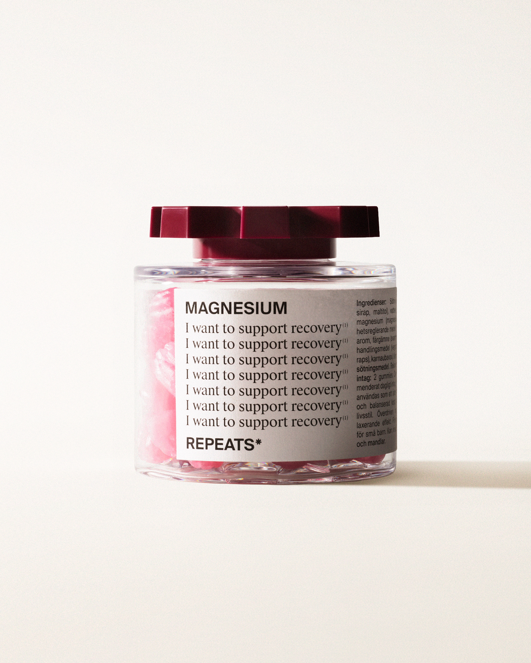 A transparent jar of REPEATS Magnesium, filled with pink gummies (supplements), sealed with a dark red, shaped lid. The jar has a white label featuring the text "Magnesium", repeated rows of "I want to support recovery", and the brand Logo
