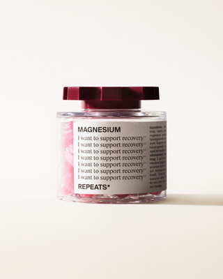 A transparent jar of REPEATS Magnesium, filled with pink gummies (supplements), sealed with a dark red, shaped lid. The jar has a white label featuring the text "Magnesium", repeated rows of "I want to support recovery", and the brand Logo