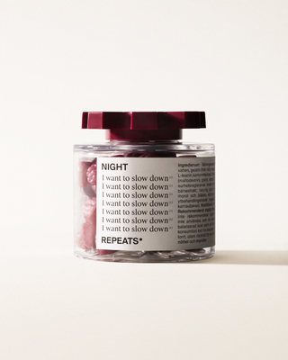 A transparent jar of REPEATS Night, filled with red gummies (supplements), sealed with a dark red, shaped lid. The jar has a white label featuring the text "Night", repeated rows of "I want to slow down", and the brand Logo