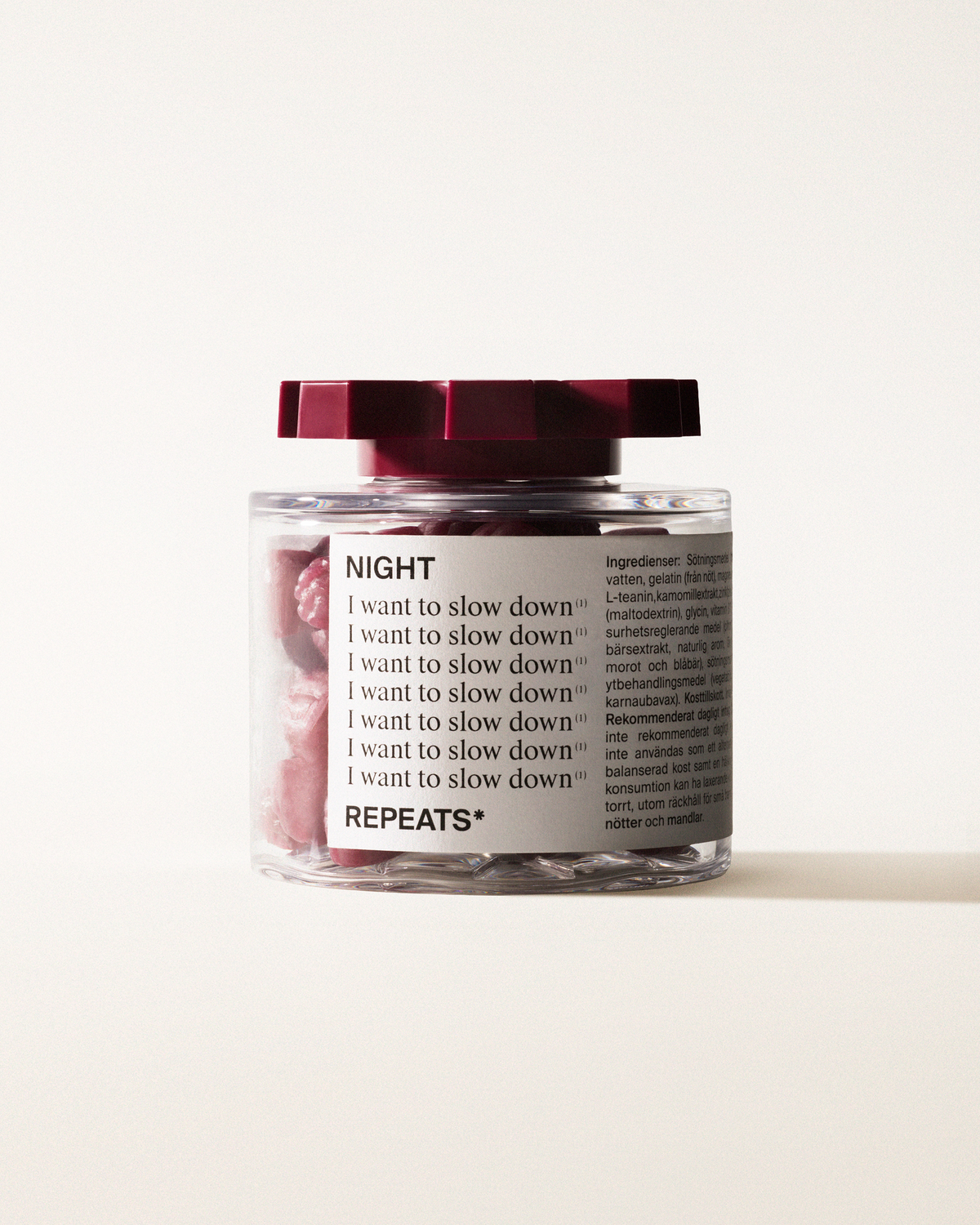 A transparent jar of REPEATS Her Daily, filled with orange gummies (supplements), sealed with a dark red, shaped lid. The jar has a white label featuring the text "Night", repeated rows of "I want to slow down", and the brand Logo