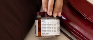 A person in a cream coat reaching for a REPEATS Skin jar beside a burgundy leather bag.