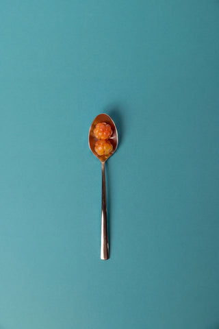 A silver spoon on a solid teal background, containing two small cloudberries.